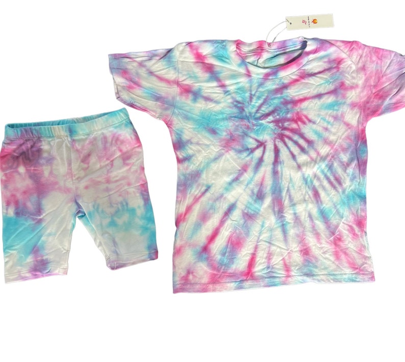 May include: A tie-dye shirt and shorts set in shades of pink, blue and white. The shirt has a round neckline and short sleeves. The shorts are biker shorts with an elasticated waistband.