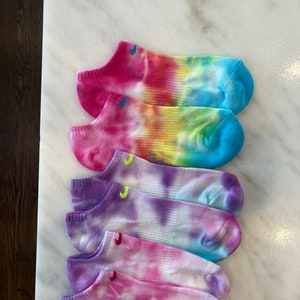 May include: Four pairs of colourful tie-dye ankle socks. The socks are white with pink, blue, purple, and yellow tie-dye patterns.