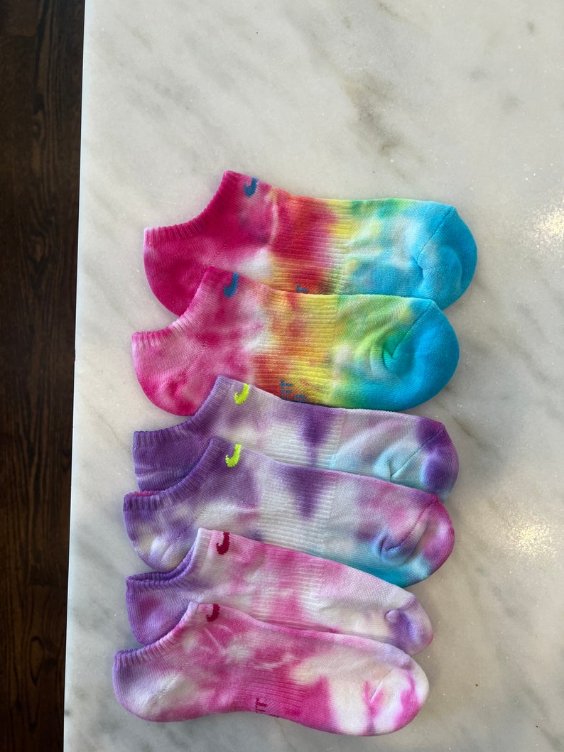 May include: Four pairs of colourful tie-dye ankle socks. The socks are white with pink, blue, purple, and yellow tie-dye patterns.