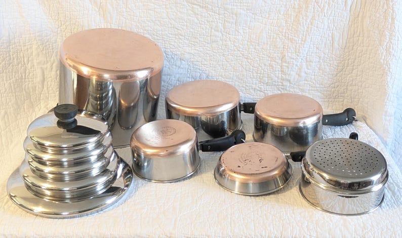 May include: A selection of stainless steel and copper-bottomed cookware, including pots, pans, and lids. The set features various sizes, with black handles and a steamer insert. The copper bottoms offer a classic aesthetic for the kitchen.