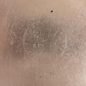 May include: Close-up of a metallic surface with a circular emblem. The emblem features text including "CO. 1870 RIVER" and "PATENT 2272609". The words "MADE UNDER PROCESS PATENT" are also visible. The surface has a brushed texture.