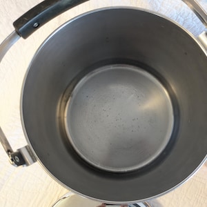 May include: A stainless steel tea kettle with a black handle and a silver handle. The kettle has a wide opening and a round base. The interior of the kettle is silver.