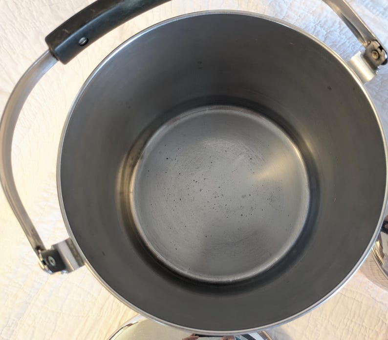 May include: A stainless steel tea kettle with a black handle and a silver handle. The kettle has a wide opening and a round base. The interior of the kettle is silver.