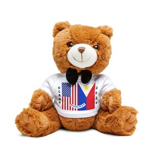 May include: A brown teddy bear wearing a white shirt with the American and Philippine flags and the text "CLASS 2024 MABUHAY". The bear is wearing a black bow tie.