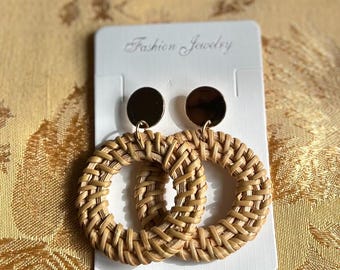 May include: A pair of woven rattan hoop earrings with gold-toned metal accents. The earrings are displayed on a white card with the text "Fashion Jewelry".