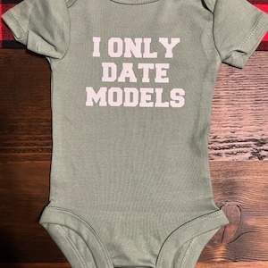 May include: A green baby onesie with the text "I only date models" printed in white.