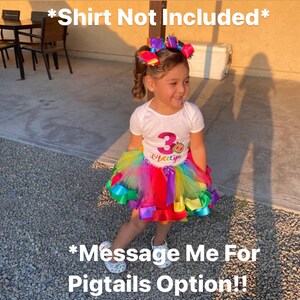 May include: A young girl wearing a white shirt with a pink and purple number 3 and the word "Happy" on it. She is wearing a rainbow tulle tutu with colorful ribbons. The girl has her hair in two pigtails with colorful bows. The text "*Shirt Not Included*" and "*Message Me For Pigtails Option!" is visible in the image.