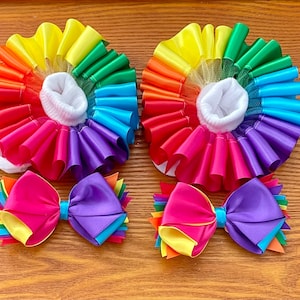 May include: Two pairs of rainbow ruffle socks with white socks and two rainbow bows. The socks are made of satin ribbon and tulle. The bows are made of satin ribbon.
