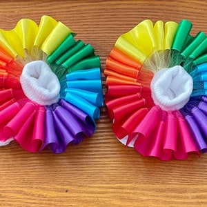 May include: A pair of rainbow-colored baby socks with a white ruffle trim and a white sock liner. The socks are made of a soft, stretchy fabric and are perfect for a baby's delicate feet.