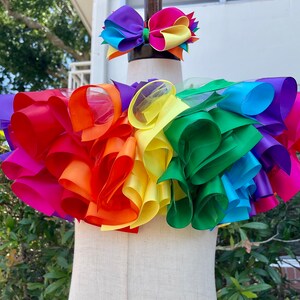 May include: Rainbow layered tulle and ribbon skirt with a matching rainbow ribbon hair bow. The skirt is made of multiple layers of tulle and ribbon in the colors of the rainbow. The hair bow is made of a single layer of ribbon in the colors of the rainbow.