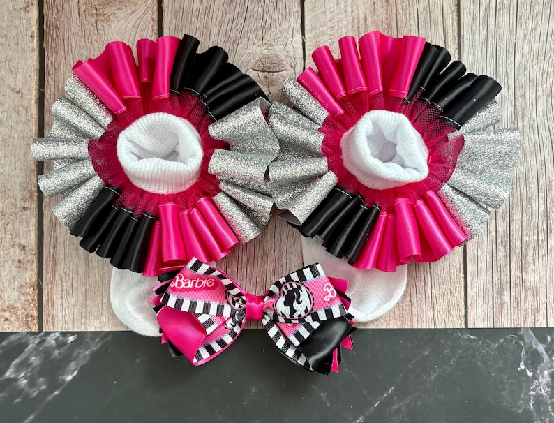 Peut inclure: Chaussettes &agrave; volants roses et noires avec des paillettes argent&eacute;es et un n&oelig;ud rose et noir avec le mot "Barbie" dessus.