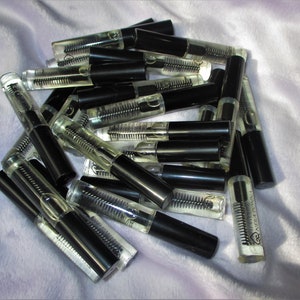 May include: A pile of clear glass bottles with black caps and a small brush applicator. The bottles contain a clear liquid. The bottles are labeled "LASH REVIVAL".