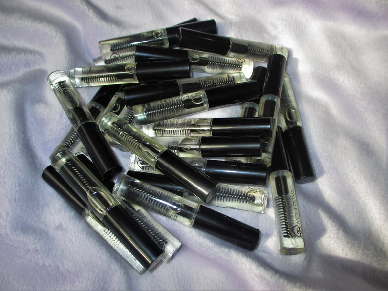 May include: A pile of clear glass bottles with black caps and a small brush applicator. The bottles contain a clear liquid. The bottles are labeled "LASH REVIVAL".