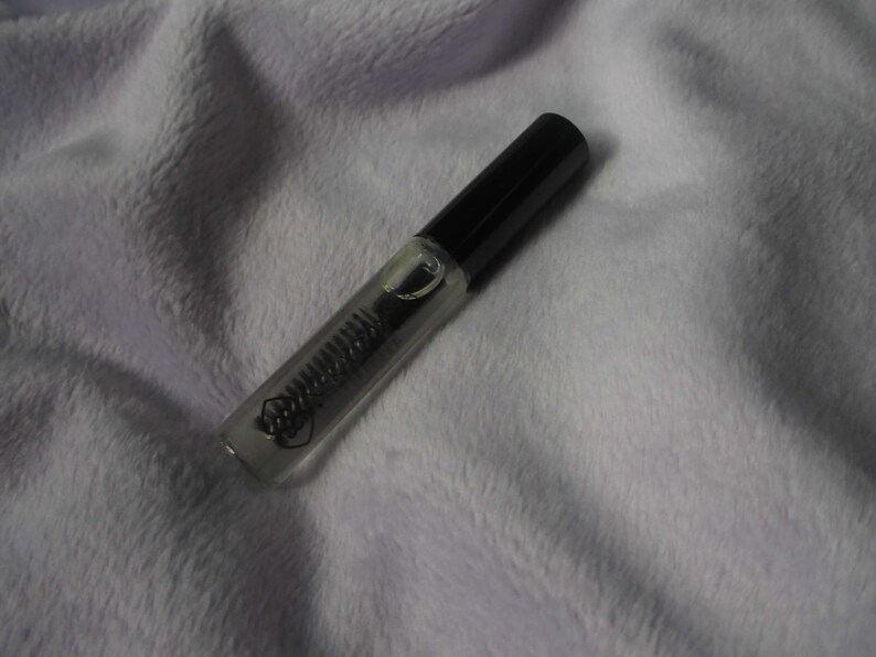 May include: A clear glass tube with a black cap containing a clear liquid. The tube is lying on a white fuzzy surface.