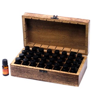 May include: A wooden box for essential oils, with a hinged lid and a metal clasp. The box is filled with small black bottles. One bottle, labelled "Rosemary Essential Oil", sits outside the box. The box is made of light brown wood.