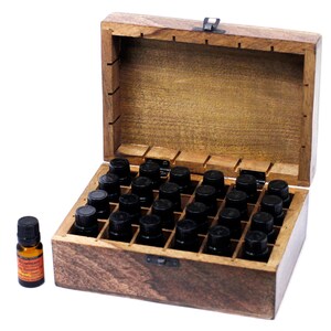 May include: A wooden essential oil storage box with an open lid, filled with small black bottles. A single bottle with a label is to the left. The box is made of light brown wood and has a metal clasp.