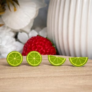 May include: Four lime-shaped decorative items. Two are circular, and two are quarter-circle wedges. The limes are bright green with a lighter green interior. The items are arranged on a light brown surface.