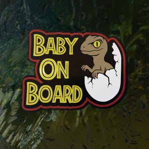 K&ouml;nnte beinhalten: Ein rechteckiger Aufkleber mit schwarzem Hintergrund und rotem Rand, der den gelben Schriftzug BABY ON BOARD zeigt. Rechts schl&uuml;pft ein braunes Cartoon-Dinosaurierbaby mit gelbem Auge aus einem wei&szlig;en, zerbrochenen Ei.