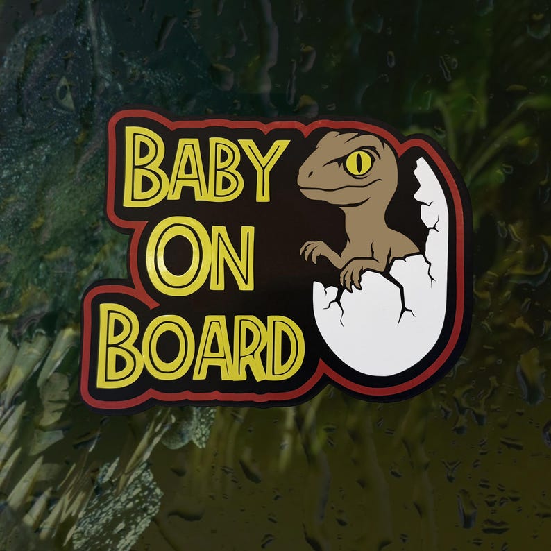 K&ouml;nnte beinhalten: Ein rechteckiger Aufkleber mit schwarzem Hintergrund und rotem Rand, der den gelben Schriftzug BABY ON BOARD zeigt. Rechts schl&uuml;pft ein braunes Cartoon-Dinosaurierbaby mit gelbem Auge aus einem wei&szlig;en, zerbrochenen Ei.