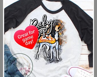 May include: White and black baseball tee shirt with a watercolor illustration of a dog wearing a vest that says "Smokey" and the text "Rocky Top". The shirt also has a red heart with the text "Great for game day!"
