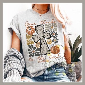 Puede incluir: Camiseta gris con un diseño de cruz y detalles florales. El texto "Give thanks to the Lord" y "Psalm 136:1" están impresos en la camiseta.