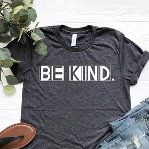 Puede incluir: Una camiseta gris oscuro con las palabras "BE KIND." impresas en blanco en la parte delantera.