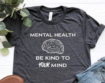 May include: A dark gray t-shirt with white text that reads "Mental Health Be Kind To Your Mind". A white outline of a brain is above the text.