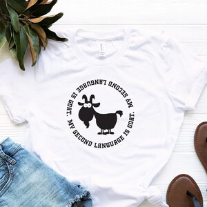 May include: White t-shirt with a black circle graphic featuring a cartoon goat and the text "My second language is goat.  My second language is goat."