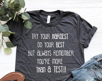 May include: A dark heather grey t-shirt with white text that reads "TRY YOUR HARDEST DO YOUR BEST BUT ALWAYS REMEMBER YOU'RE MORE THAN A TEST!!"