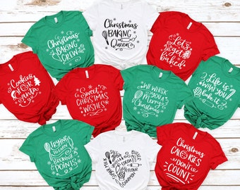 May include: A collection of Christmas-themed t-shirts in various colors, including red, green, and white. Each shirt features a unique white graphic and text related to baking and the holiday season, such as "Christmas Baking Queen" and "Cookies for Santa."