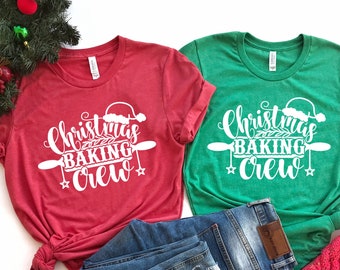 May include: Two t-shirts, one red and one green, with the text "Christmas Baking Crew" in white. The design includes a Santa hat, rolling pin, and stars. Blue jeans and a red knit hat are also visible.