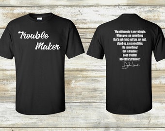 May include: Black t-shirt with white text that reads "Trouble Maker" on the front and a quote by John Lewis on the back. The quote reads: "My philosophy is very simple. When you see something that's not right, not fair, not just, stand up, say something. Do something! Get in trouble! Good trouble! Necessary trouble!"