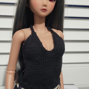 May include: A black knitted halter top with a deep V-neckline. The top is worn by a doll with long black hair and red eyes.