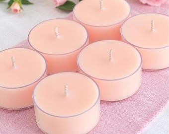 May include: A set of six round, light pink tea light candles, each encased in a clear plastic cup. Each candle features a centered, white cotton wick. The candles are arranged in a cluster, displaying a smooth, solid wax surface.