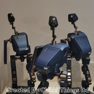 May include: Three navy blue and bronze-colored robot models with articulated limbs and head-mounted sensors. Each robot stands on a black hexagonal base. The text "MK.II" is visible on a label. The text "Created By Chikki Things Ltd" is also visible.