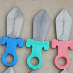May include: Six plastic toy swords with different colored handles. The swords are silver with a pointed tip and a rounded handle. The handles are blue, green, red, purple, brown, and white.