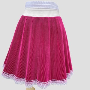 May include: A pink pleated skirt with a white waistband and white lace trim.