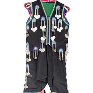 May include: A black sleeveless vest with a zipper closure and a green lining. The vest is decorated with silver coins and blue and green embroidery.