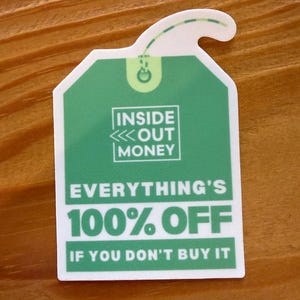 May include: A green and white sticker in the shape of a tea bag tag. The sticker has the text "INSIDE OUT MONEY" and "EVERYTHING'S 100% OFF IF YOU DON'T BUY IT". The sticker is on a wooden surface.