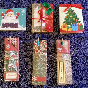 May include: A collection of Christmas-themed stationery and pencil holders. The stationery includes notebooks with Santa Claus, a Christmas tree, and gift box designs. Pencil holders are decorated with snowflakes and holiday patterns.