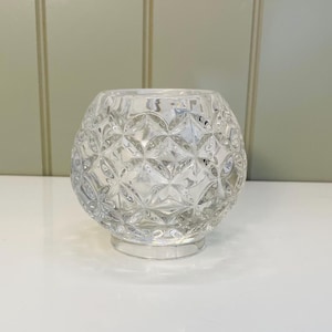 May include: A clear glass candle holder with a geometric pattern. The holder has a round base and a wide, open top.