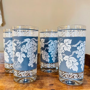 May include: Set of four blue glass tumblers with a white grapevine design. The glasses have a white band around the top and bottom.