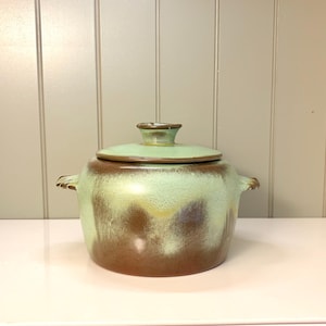 May include: A ceramic cooking pot with a lid. The pot is a rounded shape with two handles and a lid with a small knob. The pot has a brown base that fades into a light green color. The lid is light green.
