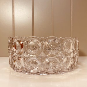 May include: A clear glass bowl with a decorative pattern of circles. The bowl is made of thick glass and has a rounded shape.