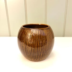 May include: A brown ceramic vase with a textured, vertical striped pattern. The vase has a rounded shape and a dark brown interior. The exterior has a glossy finish, reflecting light. This decorative vase is suitable for home decor.