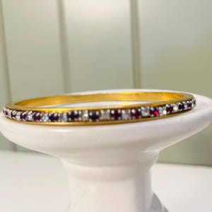 May include: A gold bangle bracelet with a single row of alternating clear and red rhinestones.