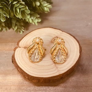 May include: A pair of gold tone earrings with clear teardrop shaped crystals and a small pearl accent.