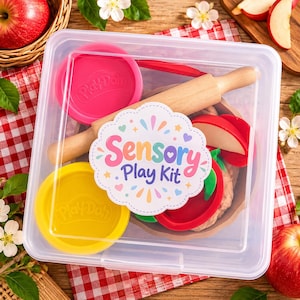 May include: A clear plastic storage container holding a sensory play kit. Inside are a wooden rolling pin, a pink Play-Doh lid, a yellow Play-Doh lid, and red apple-shaped cutters. A white label on the lid reads Sensory Play Kit in colorful text.