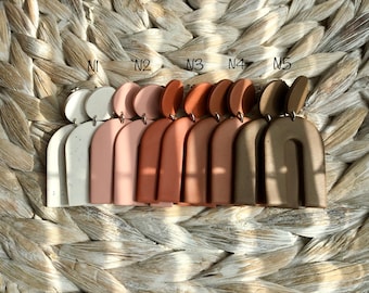 May include: Five pairs of statement earrings with a modern arch design. The earrings are made of polymer clay and come in five different colors: white, pink, terracotta, brown, and gray.