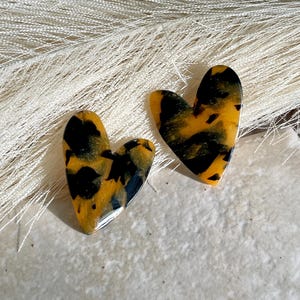 May include: A pair of heart-shaped earrings with a tortoiseshell pattern in shades of brown, yellow, and black.